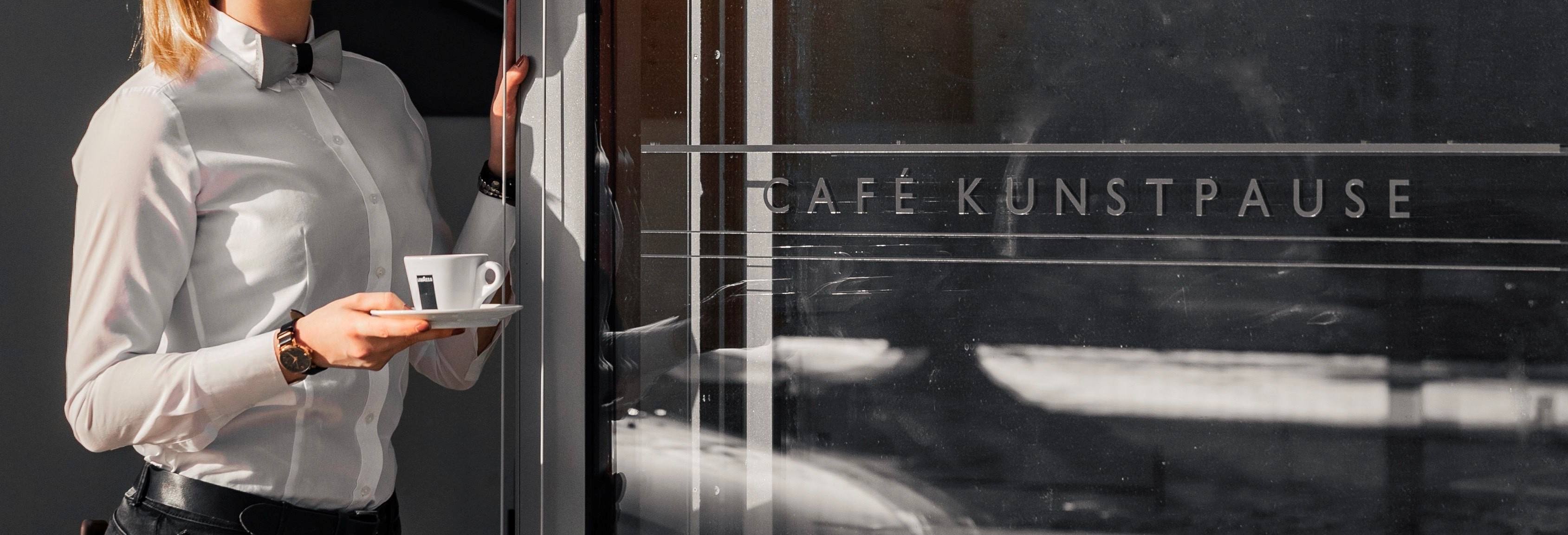 Servicekraft mit Kaffeetasse an der Glastür mit der Aufschrift Café Kunstpause