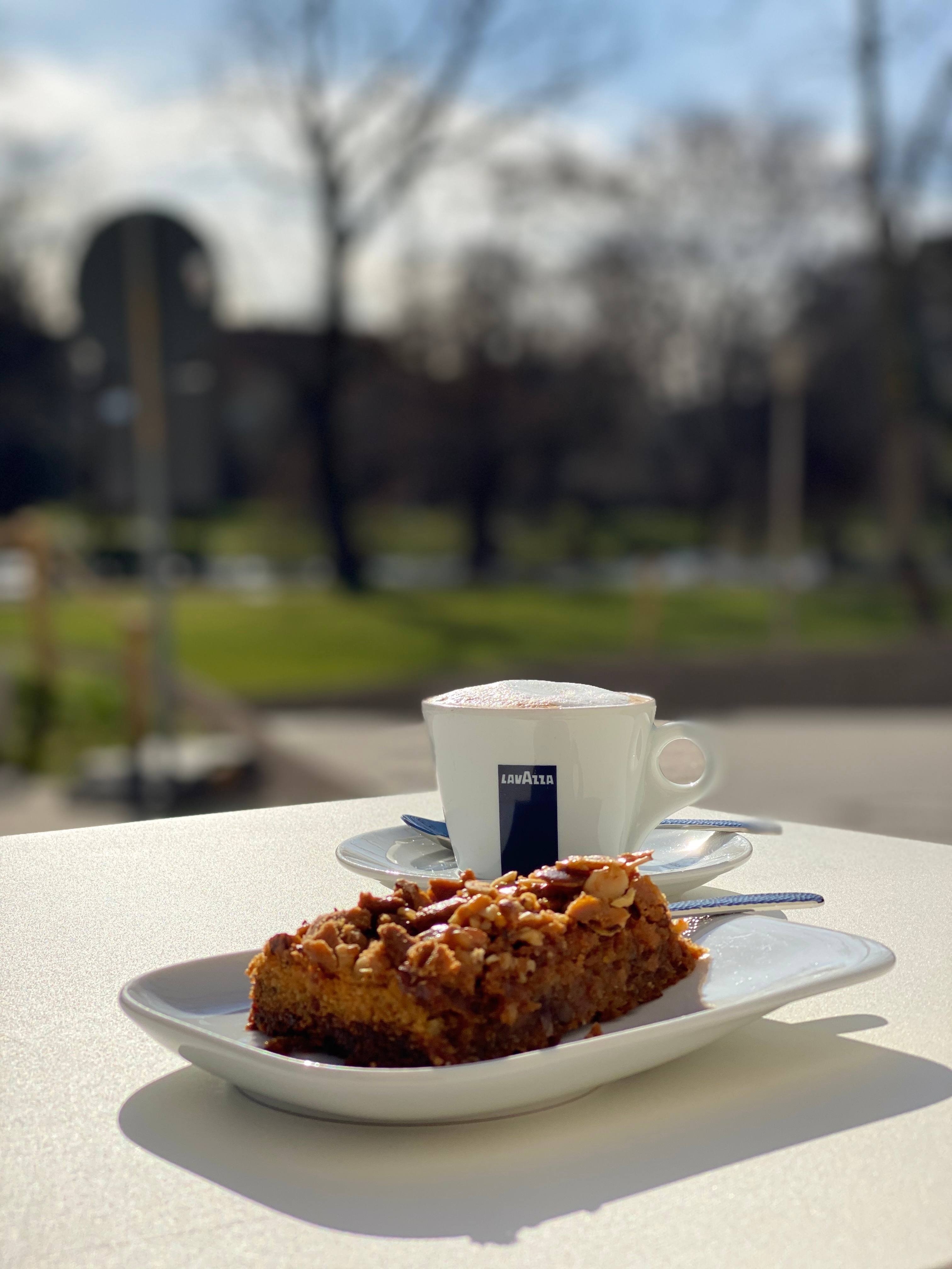 Kuchen und Kaffee auf einem weißen Tisch auf der Terrasse, dahinter der Weimarhallenpark