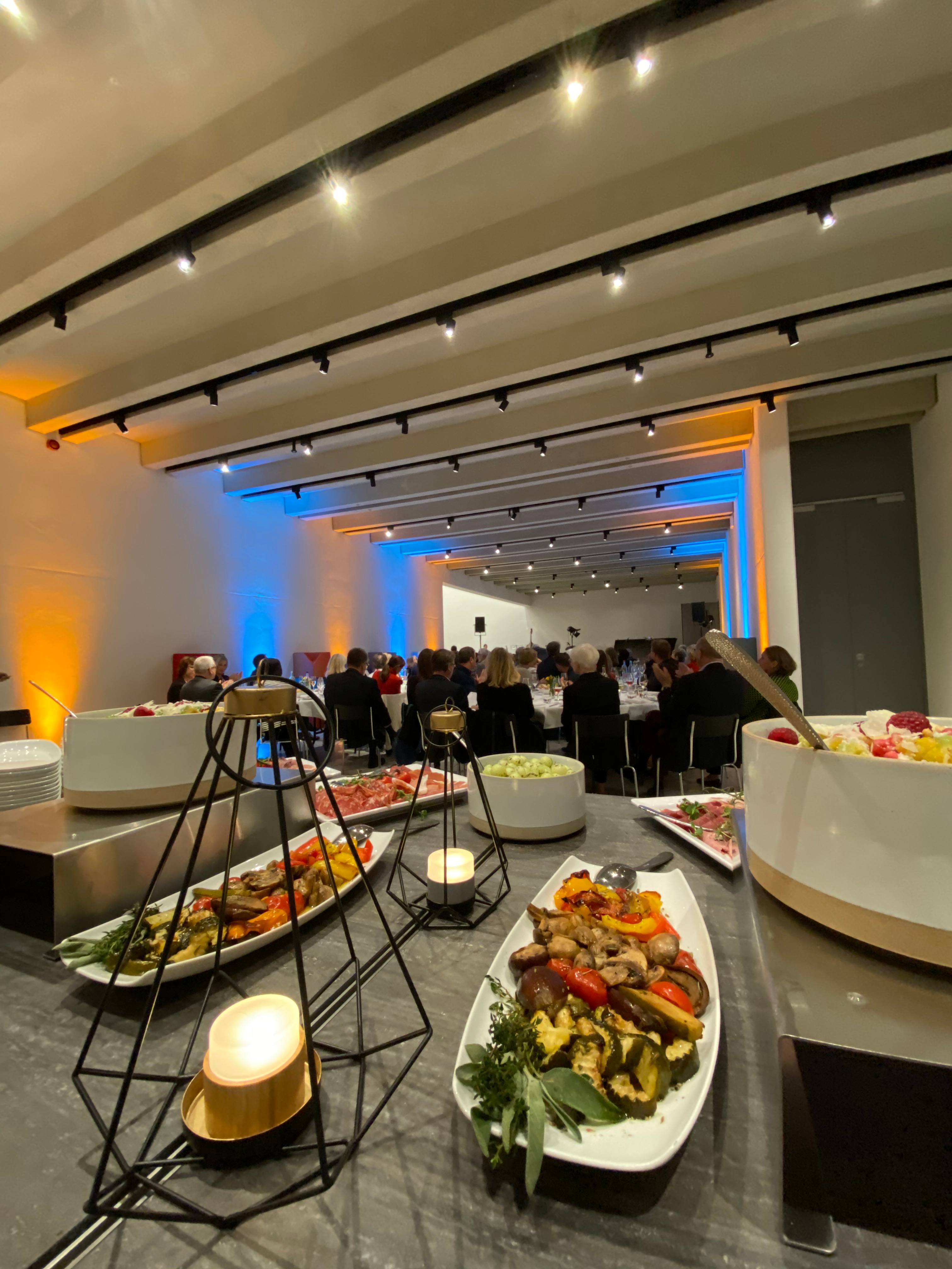 Buffet mit Salaten und Antipasti, im Hintergrund Gäste im abendlich beleuchteten Raum
